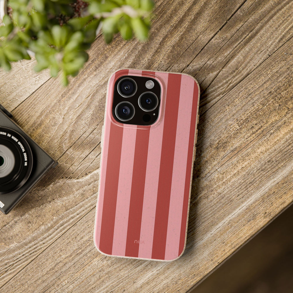 Pink striped eco-friendly iPhone case on wooden table, compatible with many models. Durable and biodegradable with a frosted finish.
