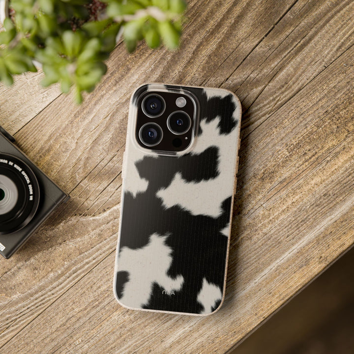 Eco-friendly biodegradable iPhone case in stylish cow print on wooden table, compatible with many iPhone and Samsung models.