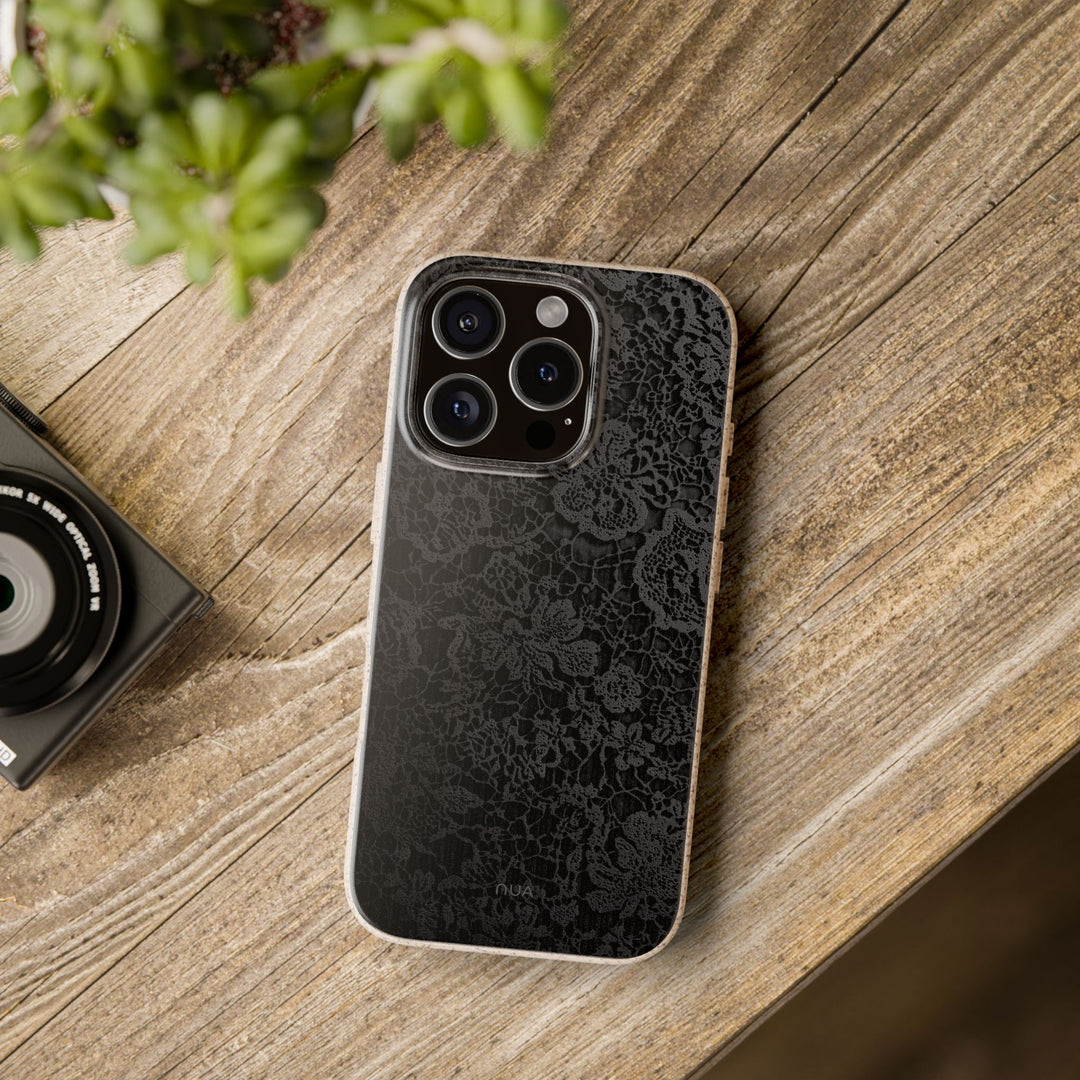 Noir Lace eco-friendly iPhone cover with black lace design on wooden table, durable for many smartphone models.